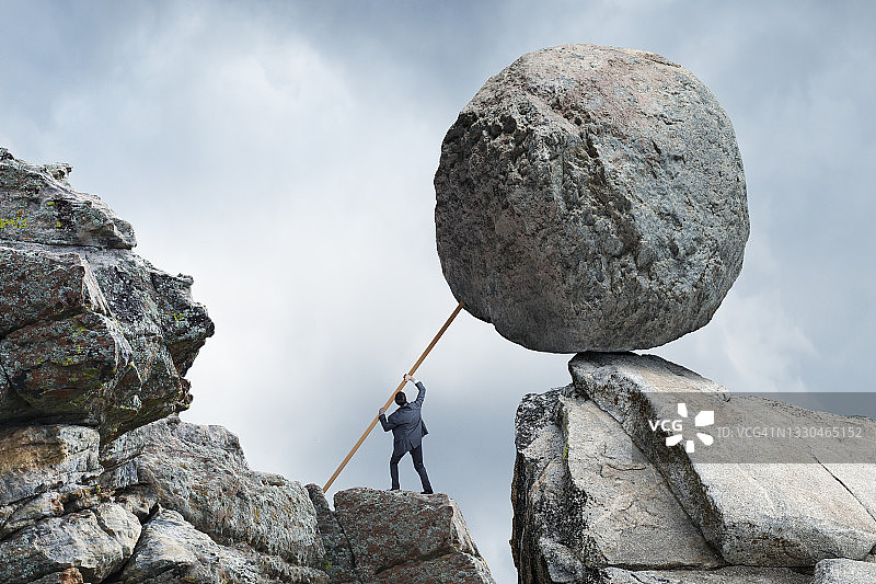 男人试图用木板支撑大圆石图片素材