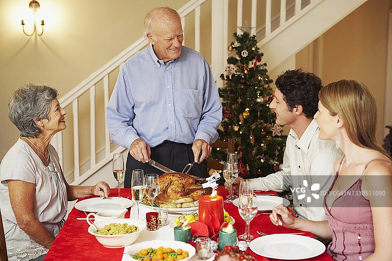 圣诞晚餐上为家人切火鸡的年长男人图片素材