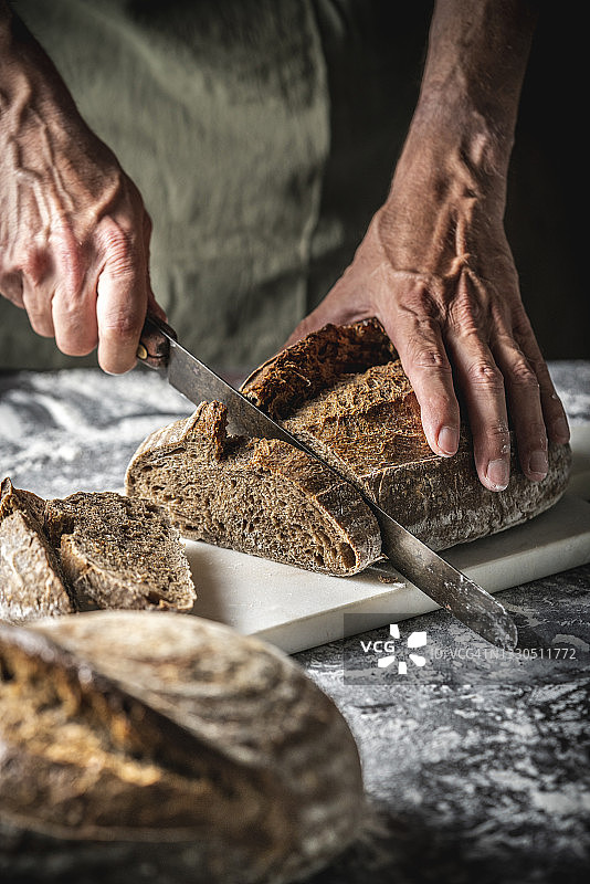 男人在砧板上切割全麦自制德式酸面包片图片素材