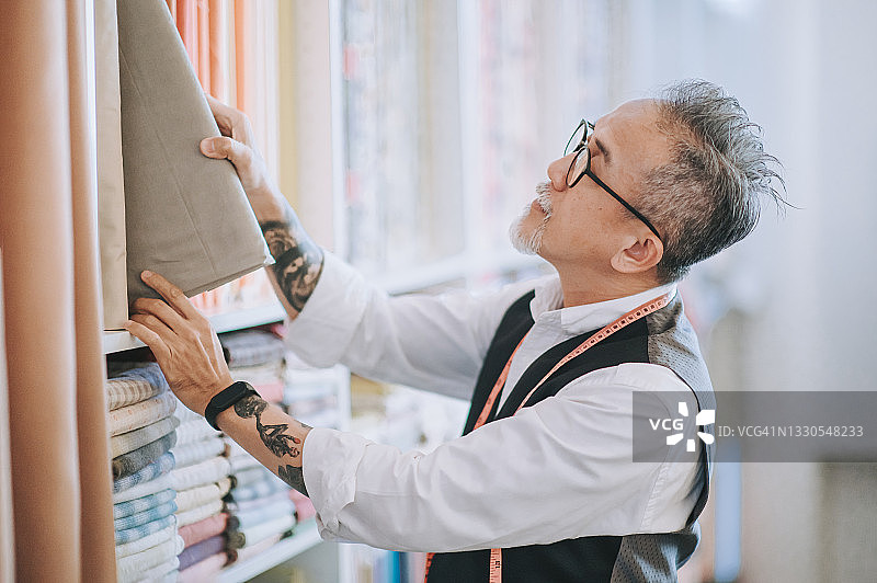 亚洲华人裁缝男面部毛发检查面料服装在工作室工作室图片素材