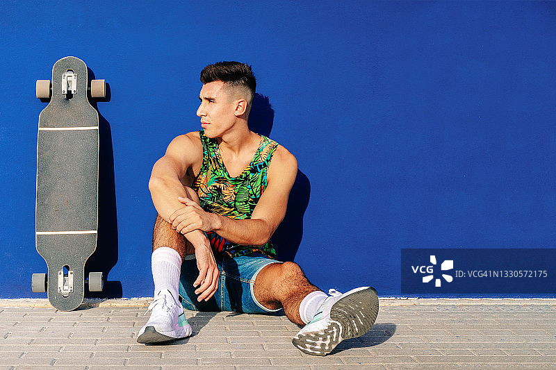 身穿牛仔服的年轻白人男子，拿着滑板，站在蓝色背景前图片素材