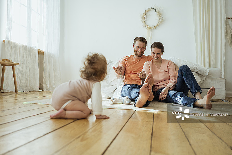 微笑的父母呼唤在家爬行的女儿图片素材