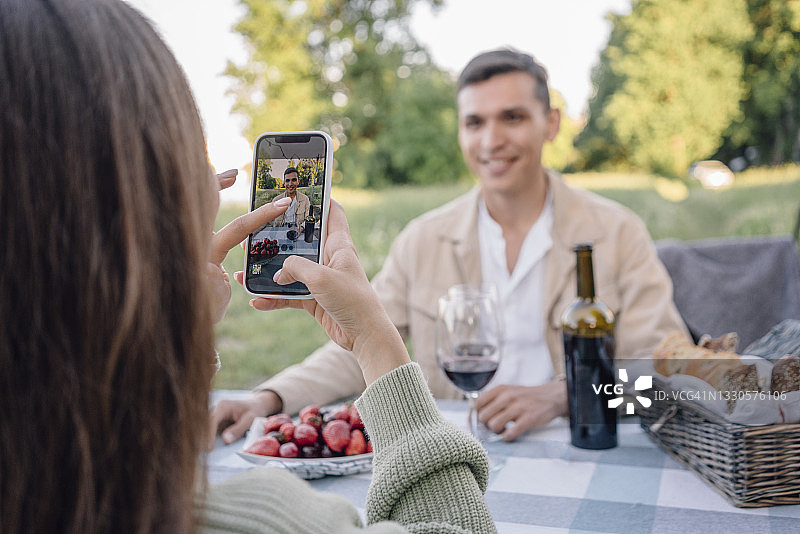 年轻女人拍摄坐在桌旁的男友图片素材