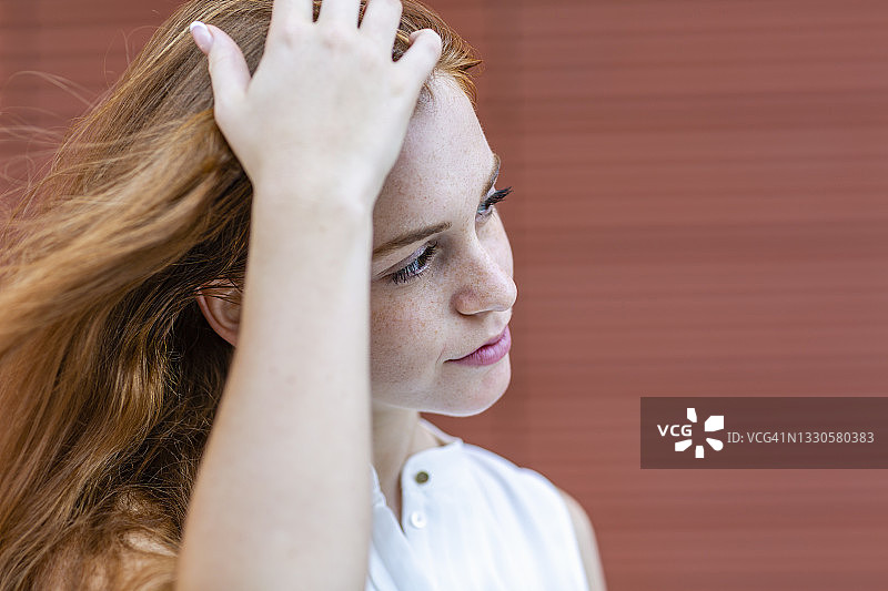 红发女自由职业者手扶头发，望向墙边图片素材