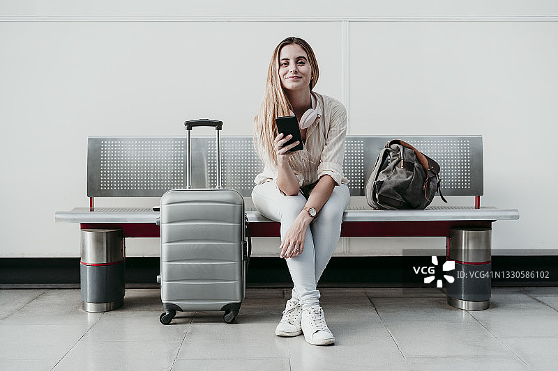 在车站坐在行李旁玩手机的美丽女人图片素材