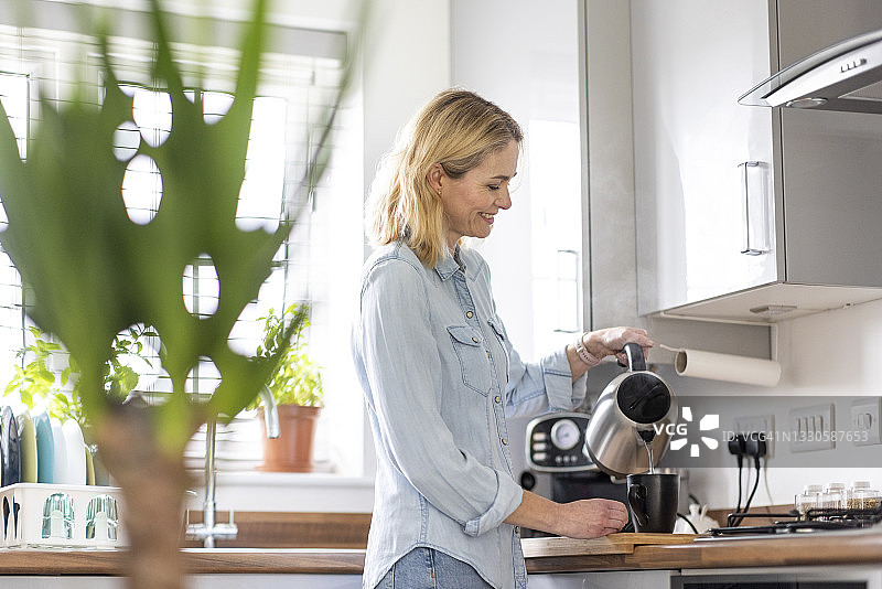 微笑的女人在家里厨房准备茶，倒水入杯图片素材