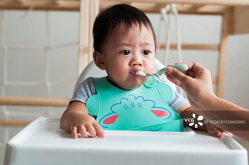 东南亚宝宝坐在高脚椅上，在母亲的帮助下吃饭图片素材