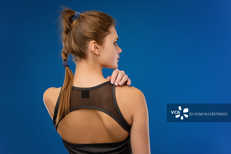 蓝色背景下的年轻女运动员的背面图片素材
