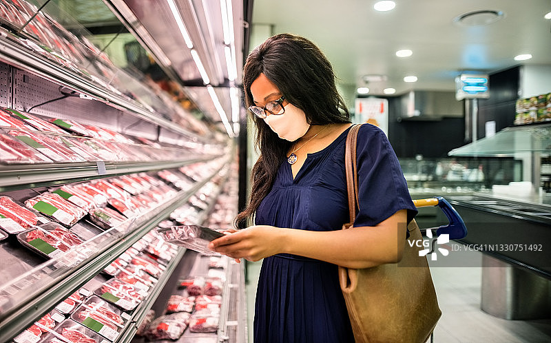 在超市里，戴着口罩的女人正在选择要购买的商品图片素材