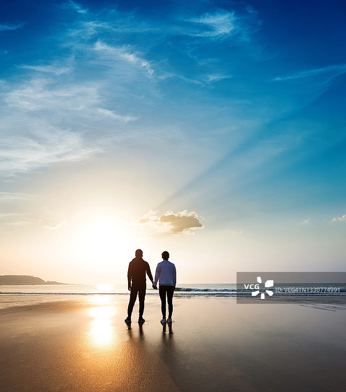 浪漫情侣在日落时分站在海滩上图片素材