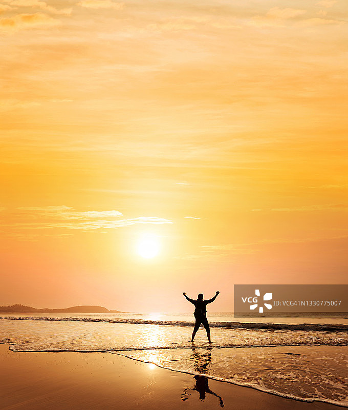 日落时分，站在海滩上举起双臂的男人们图片素材