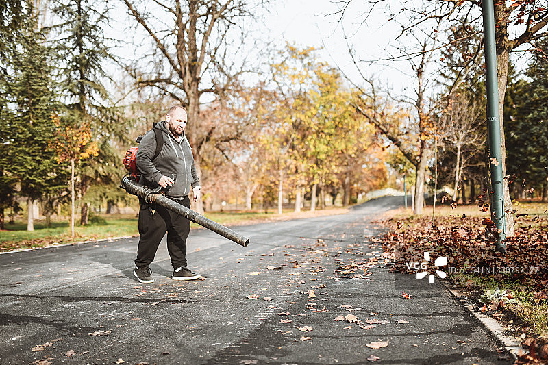 专心吹公园落叶的光头男工人图片素材