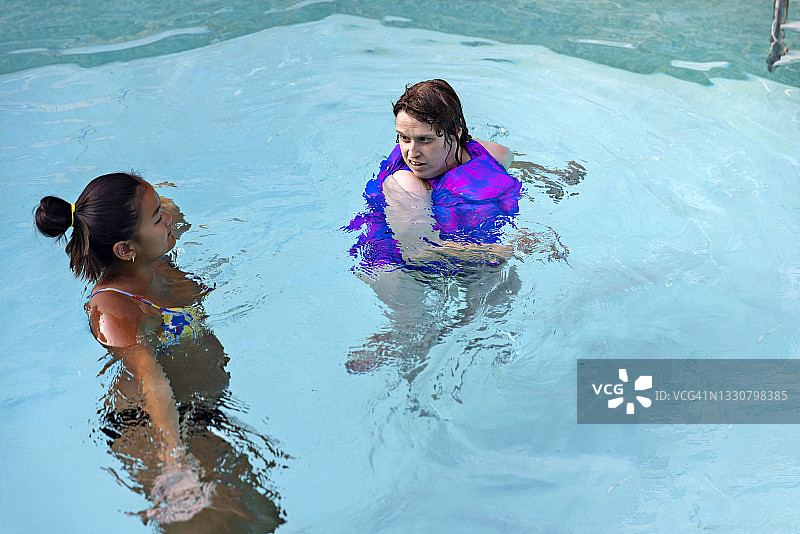 残疾年轻女性在家庭泳池独立游泳，看向护理人员图片素材