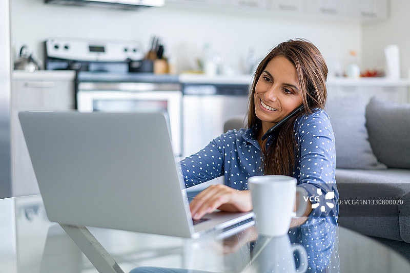 忙碌的女性在家工作，使用笔记本电脑并打电话图片素材