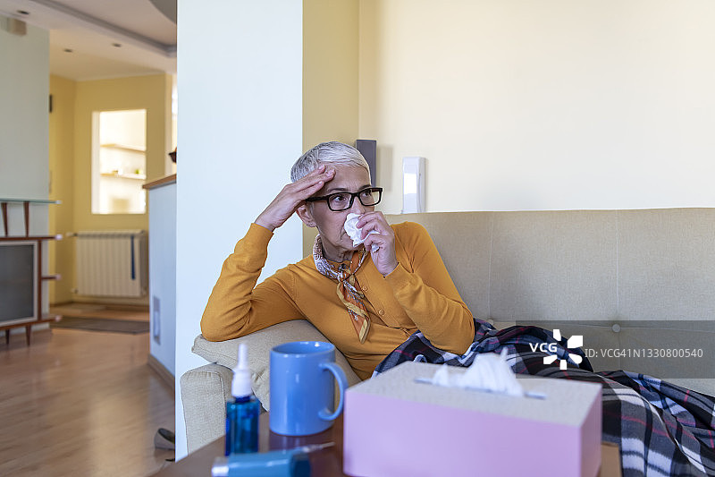 患流感的年长女人躺在家里，对着纸巾打喷嚏图片素材