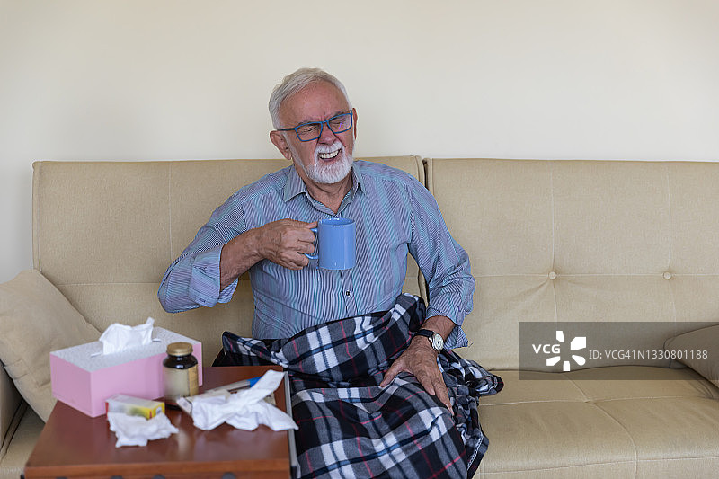 患流感病毒的老年男人正在服用药物并喝热饮图片素材