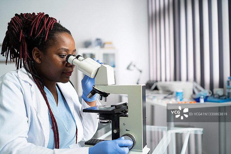 穿实验服和防护口罩的非裔美国女科学家或研究生在现代实验室工作图片素材