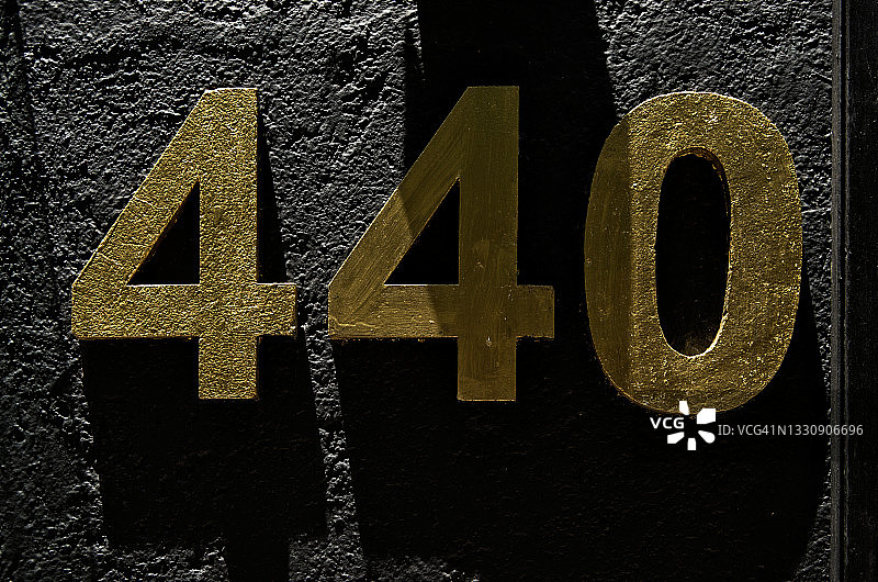 黑色水泥墙上凸起的金色数字门牌号码440图片素材