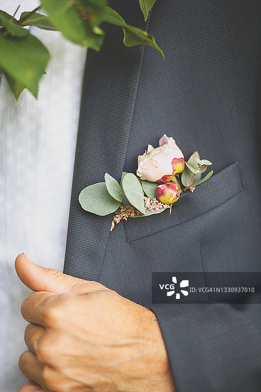 新郎身穿白色衬衫，系着领结，穿着考究的黑色西装，胸前别着粉红色玫瑰和绿叶组成的美丽胸花，婚礼主题图片素材