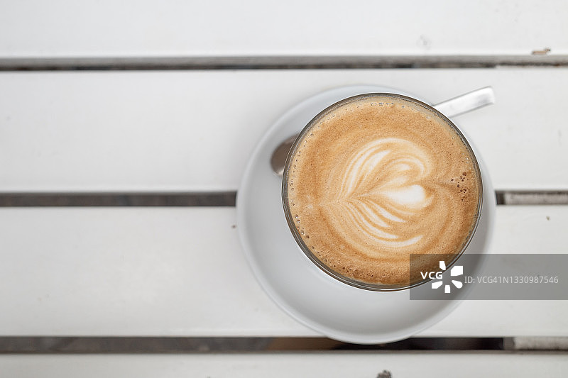户外白色木桌上的心形拉花拿铁咖啡杯图片素材