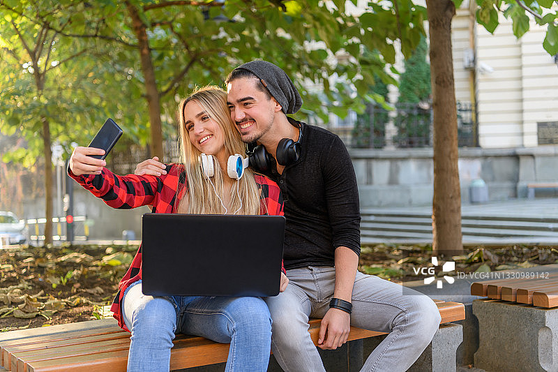 在公园木凳上用笔记本电脑工作的年轻学生情侣图片素材