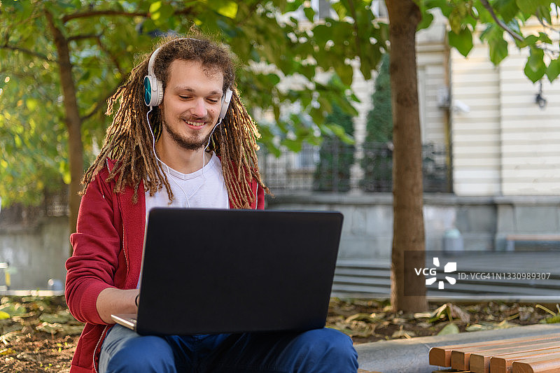 坐在公园长椅上用笔记本电脑工作的英俊青年图片素材
