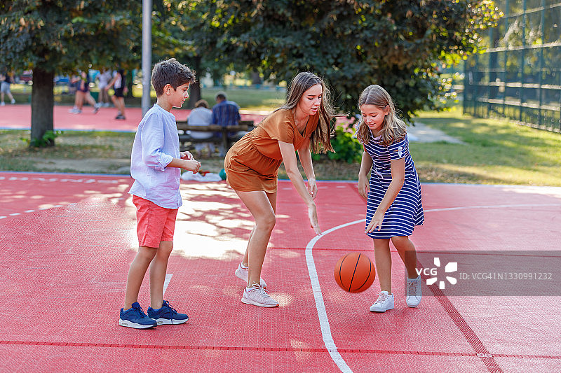 母亲在游乐场和可爱的儿子女儿一起打篮球图片素材