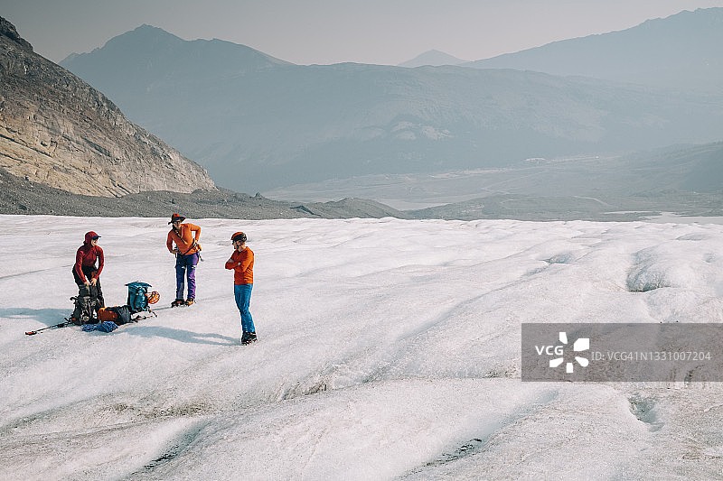三位登山者在加拿大阿尔伯塔省班夫附近的阿萨巴斯卡冰川休息图片素材
