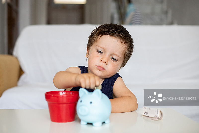 小男孩往蓝色小猪储蓄罐里投币图片素材