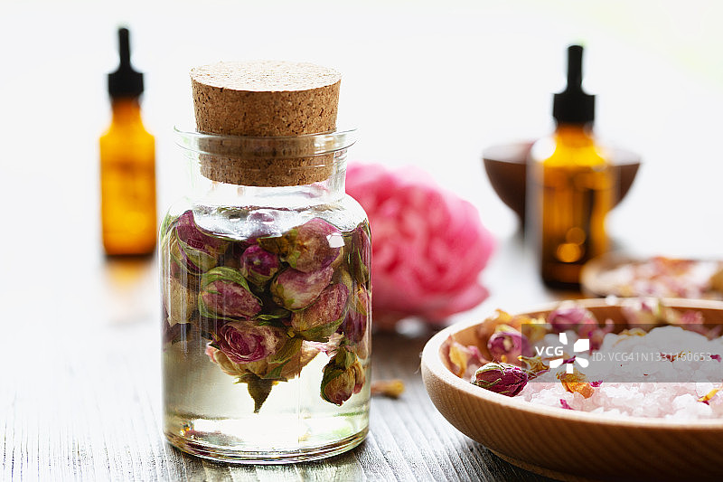 芳香疗法：按摩精油与干燥玫瑰花蕾和玫瑰香海盐木碗图片素材