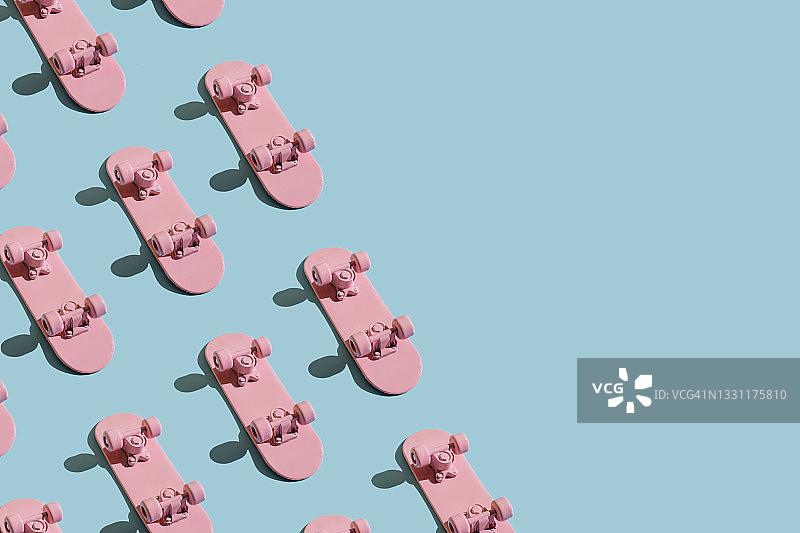 蓝色背景上的粉色滑板图案。极简创意概念。平铺，俯视，留白。青年极简运动风夏季乐趣概念。极限生活方式。图片素材