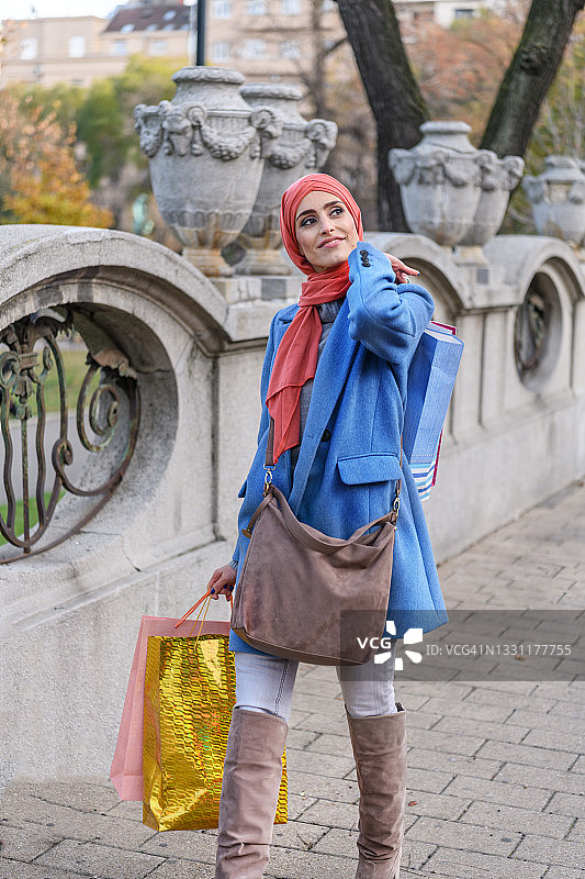 一位穆斯林女士在城市街区购物，手提纸袋图片素材
