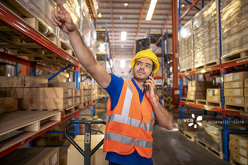 年轻男人穿安全夹克 holding 数字平板电脑站在工厂仓库的肖像图片素材