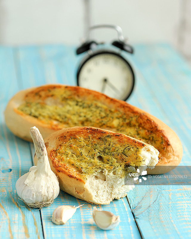 大蒜莳萝白面包，木制乡村风格桌上的面包，配有复古闹钟，柔焦，小吃时间，竖版图片素材