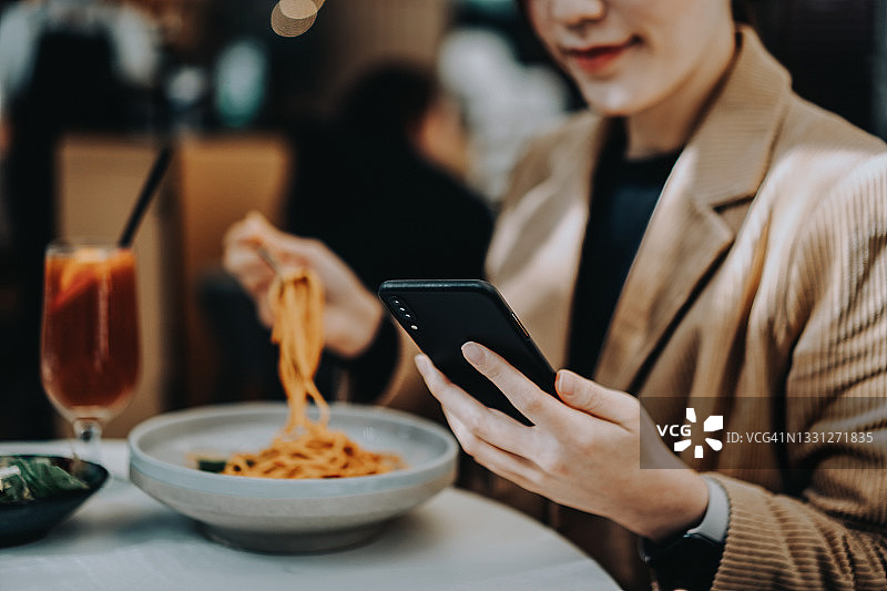 年轻亚洲女人咖啡馆午餐，使用智能手机图片素材