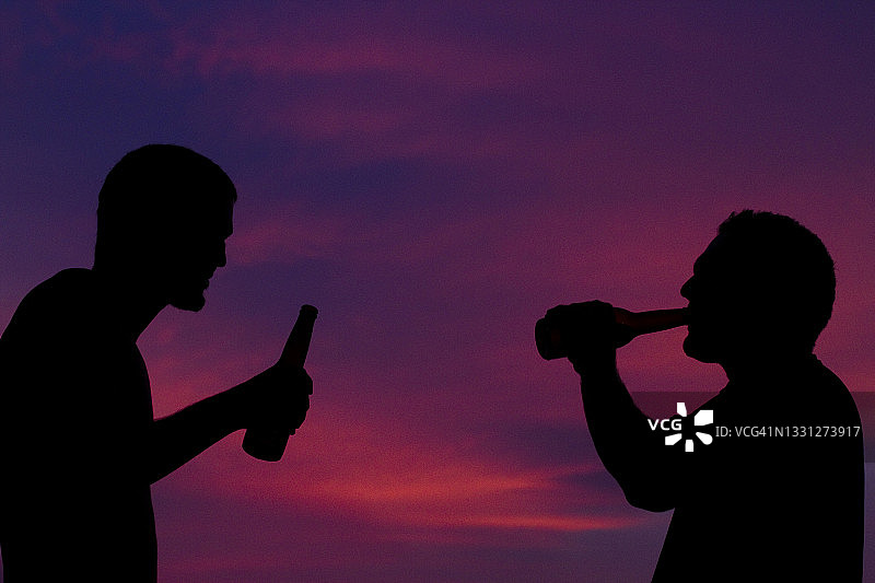 两名冲浪者在墨西哥帕斯夸莱斯冲浪一天后，一边喝啤酒一边欣赏日落图片素材