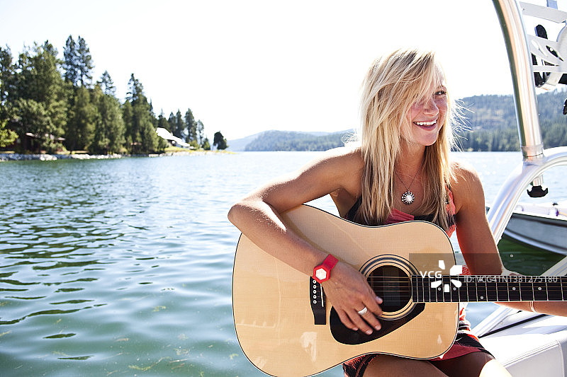 年轻女人在爱达荷州湖上的滑水艇上笑着弹吉他图片素材