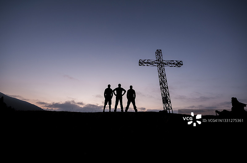 三个男孩站在意大利奥索拉山顶十字架旁的轮廓图片素材