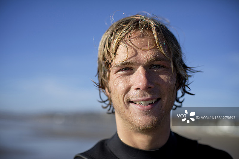 阳光明媚的一天，在加利福尼亚州圣地亚哥太平洋海滩的年轻冲浪者面带微笑直视镜头图片素材