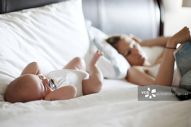 婴儿在床上放松，母亲正在读书（浅景深）图片素材