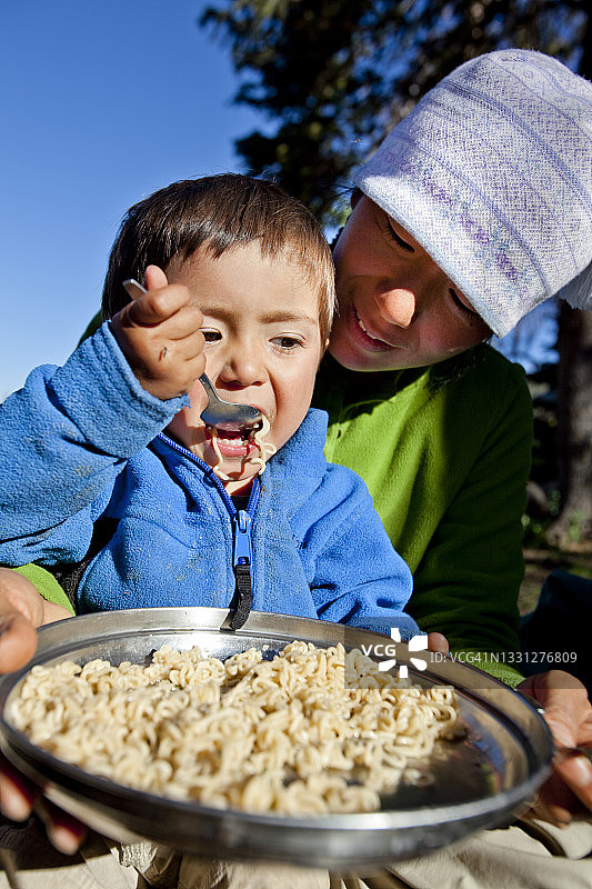 小男孩坐在妈妈的腿上，在乡村吃面条图片素材