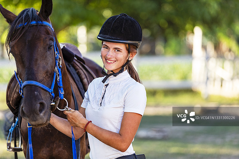 年轻女子身着骑马装备抚摸她的马图片素材