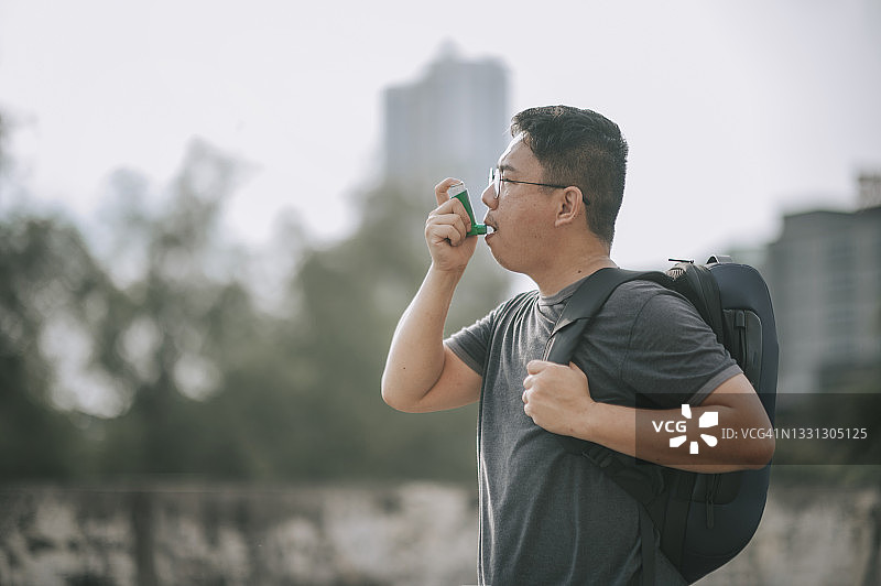 日落时分使用哮喘吸入器的亚洲中年男子图片素材