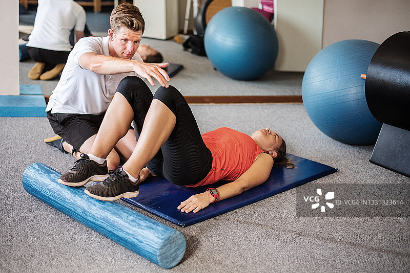 理疗师观察患者在其诊所的地板上做运动图片素材