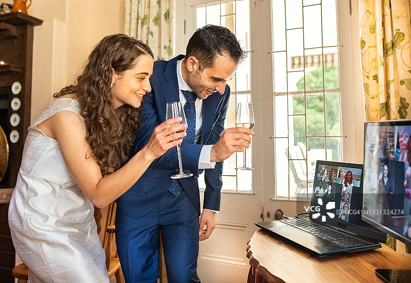 微笑的新婚夫妇在笔记本电脑上与在线观看的客人敬酒图片素材