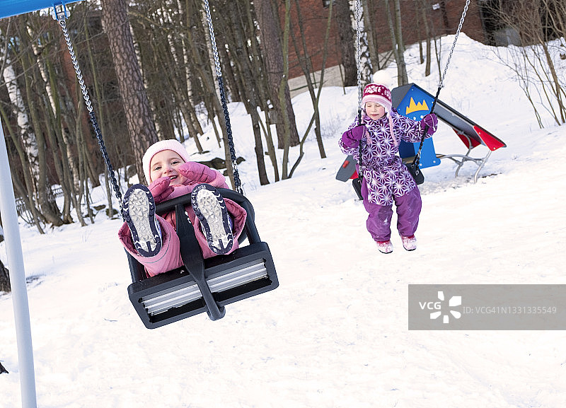 冬日，两个白人小女孩在荡秋千，在游乐场快乐地交流玩耍。图片素材