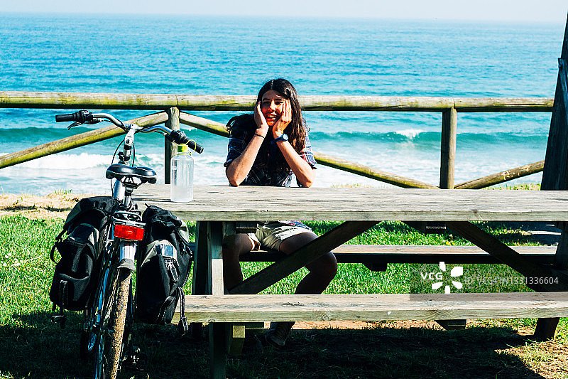 年轻女人坐在海边木桌旁，自行车放在桌上图片素材