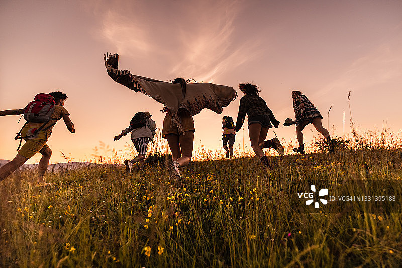 在日落时分在草地上奔跑的无忧无虑的徒步旅行者的背影。图片素材