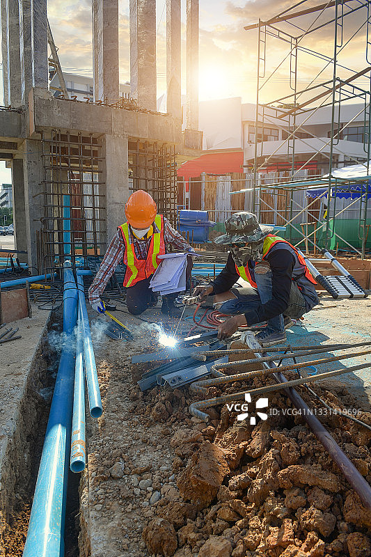 在泰国，工头在建筑工地上测量一块金属，一名工人焊接一块金属图片素材