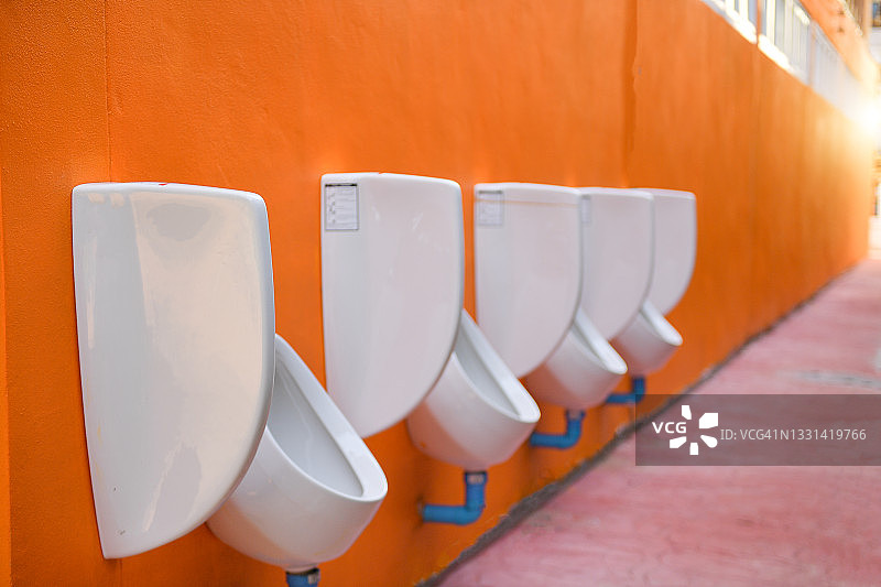 挂在橙色墙上的一排公共小便池图片素材